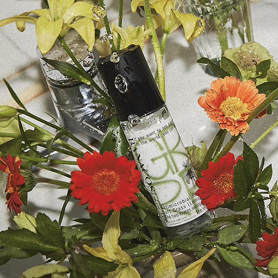 鮮やかな赤とオレンジの花、緑の葉と水滴で飾られた透明なガラスボトル